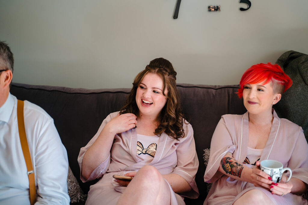 Two women in pink robes laughing on black sofa