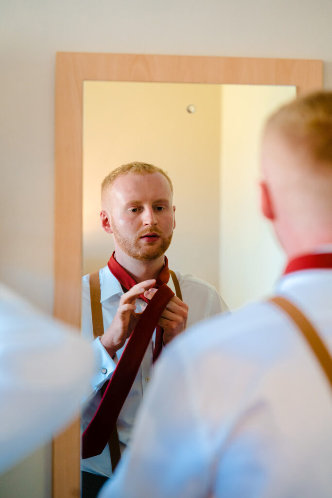 Man adjusting red tie while looking in mirror