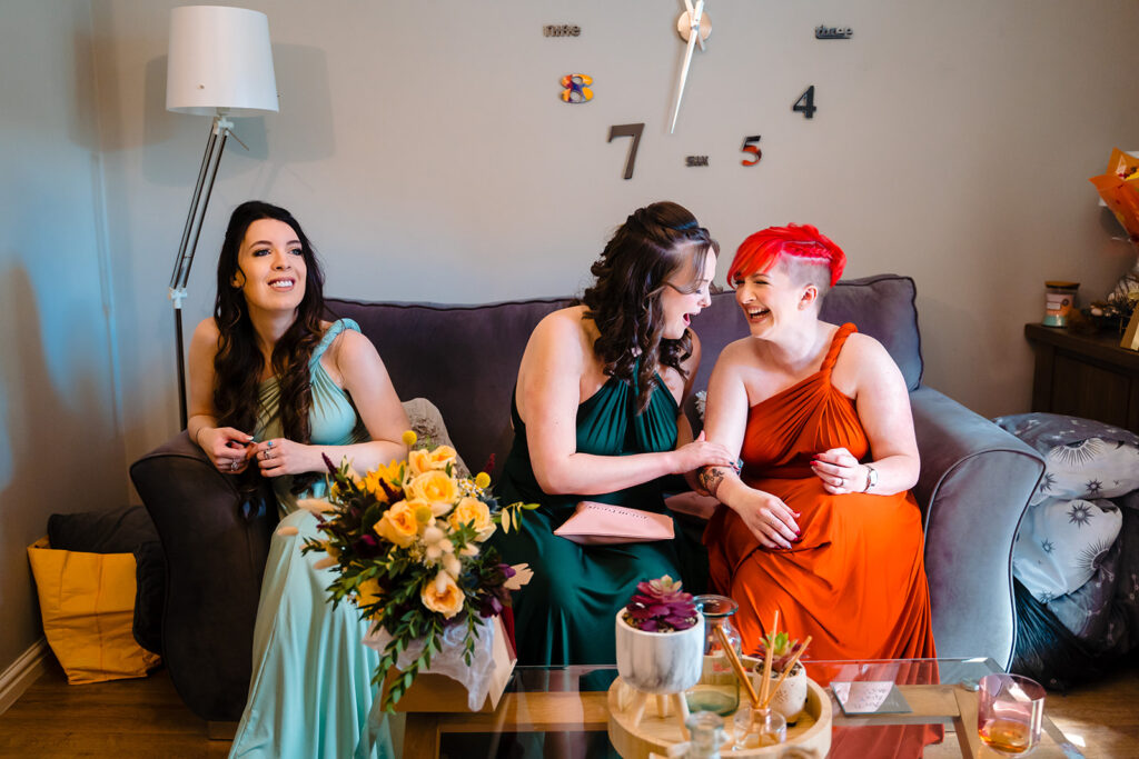 Three women in colourful dresses laughing on sofa together