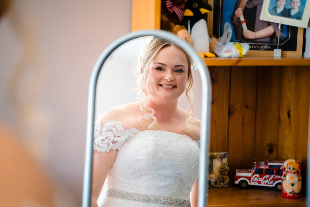 Bride in white lace dress smiling in oval mirror reflection