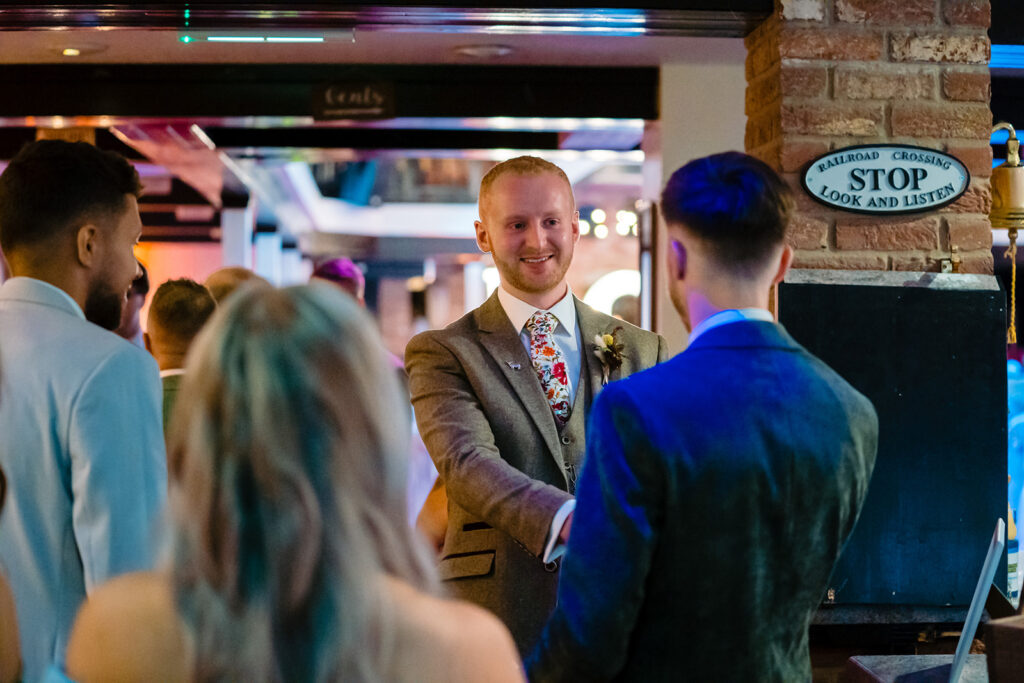 Groom in brown suit greeting guests at wedding reception
