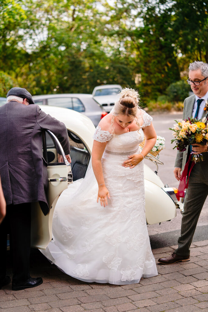 Bride in white dress exiting vintage car at wedding