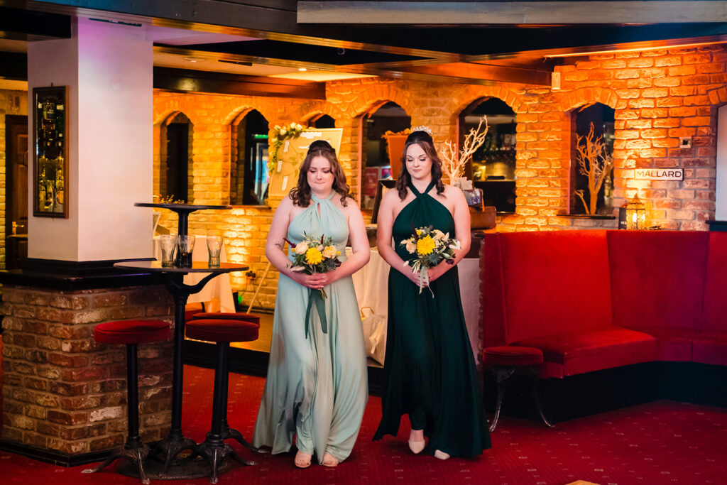 Two women in formal dresses holding bouquets indoors