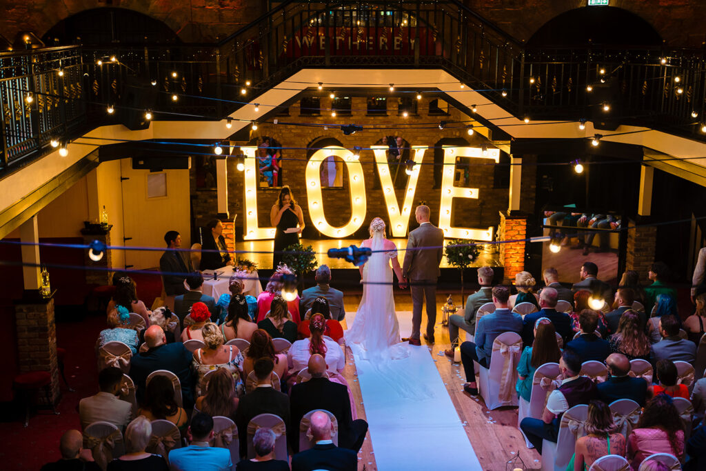 Wedding ceremony with large illuminated LOVE sign indoors