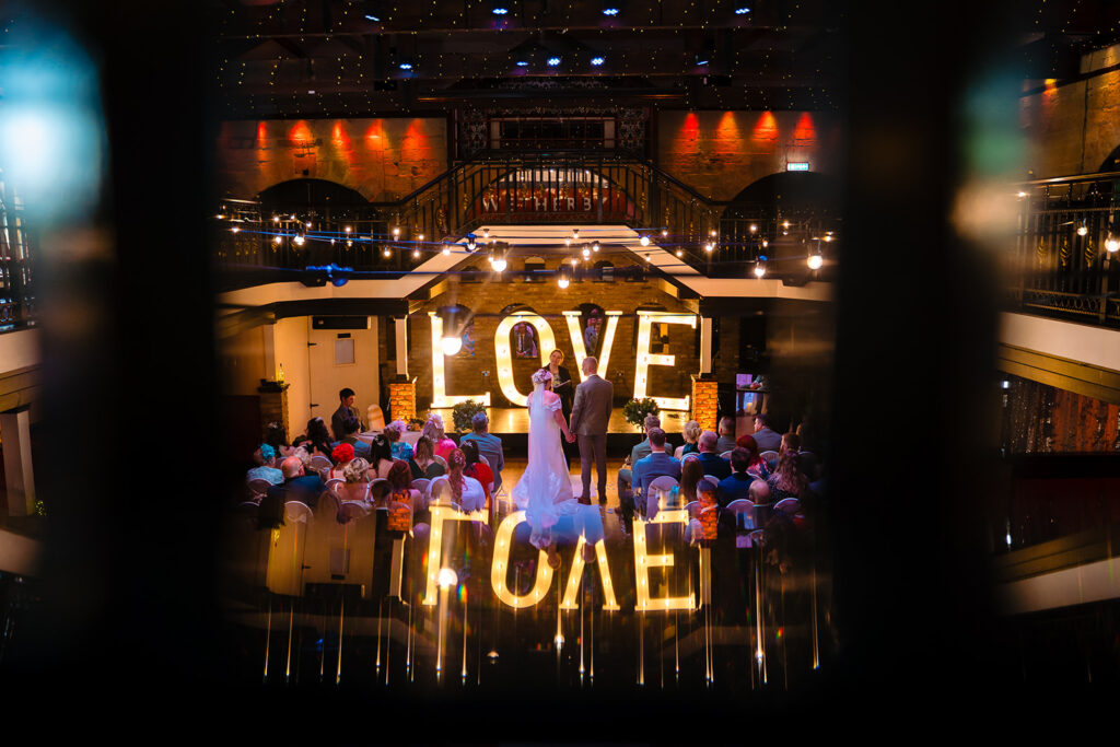 Indoor wedding ceremony with illuminated LOVE signs and guests