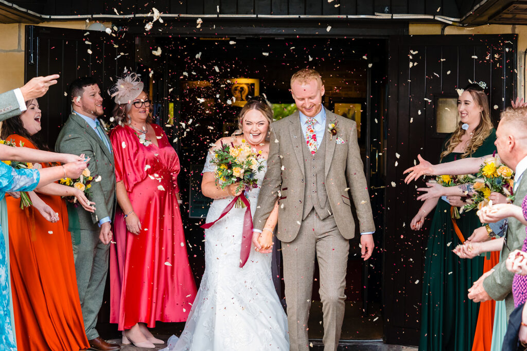 Bride and groom confetti throw with wedding guests celebrating