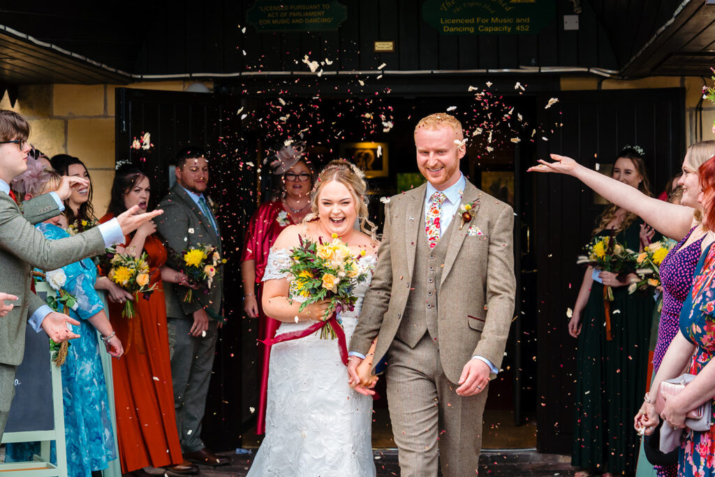 Newlyweds walk through confetti shower with smiling wedding guests