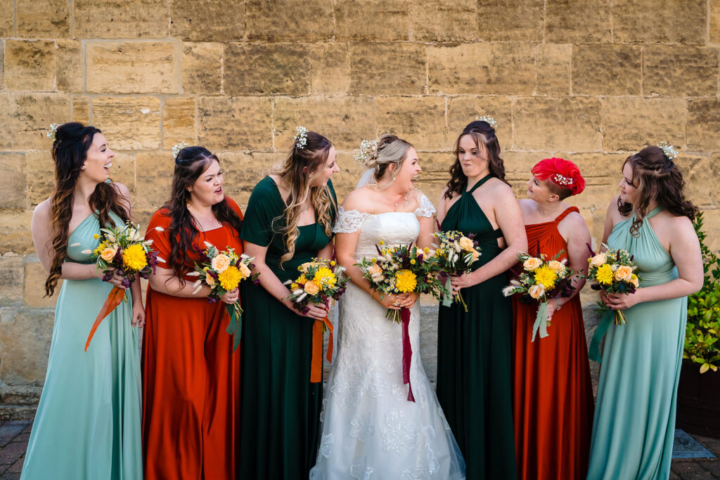 Bride and bridesmaids holding flowers against stone wall