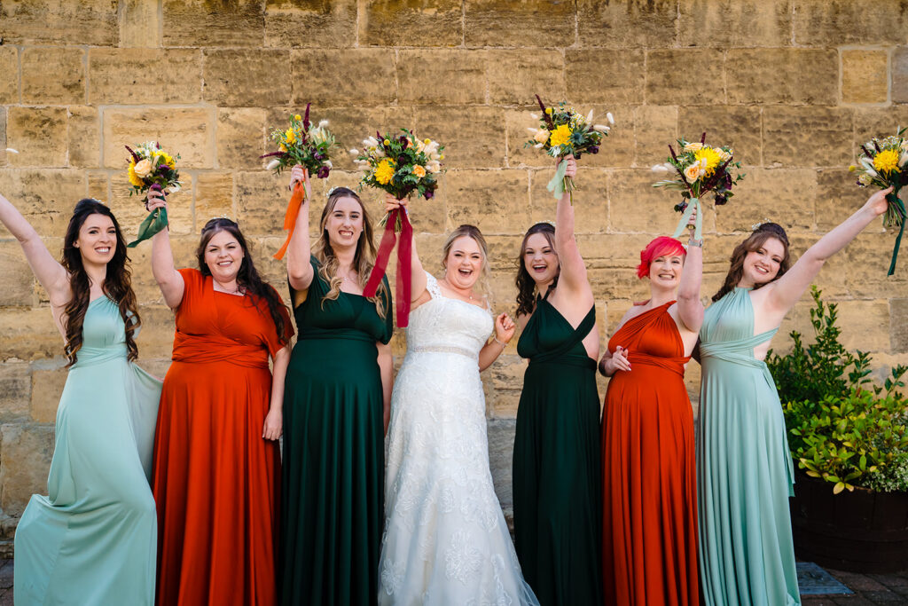 Bride and bridesmaids holding bouquets against stone wall