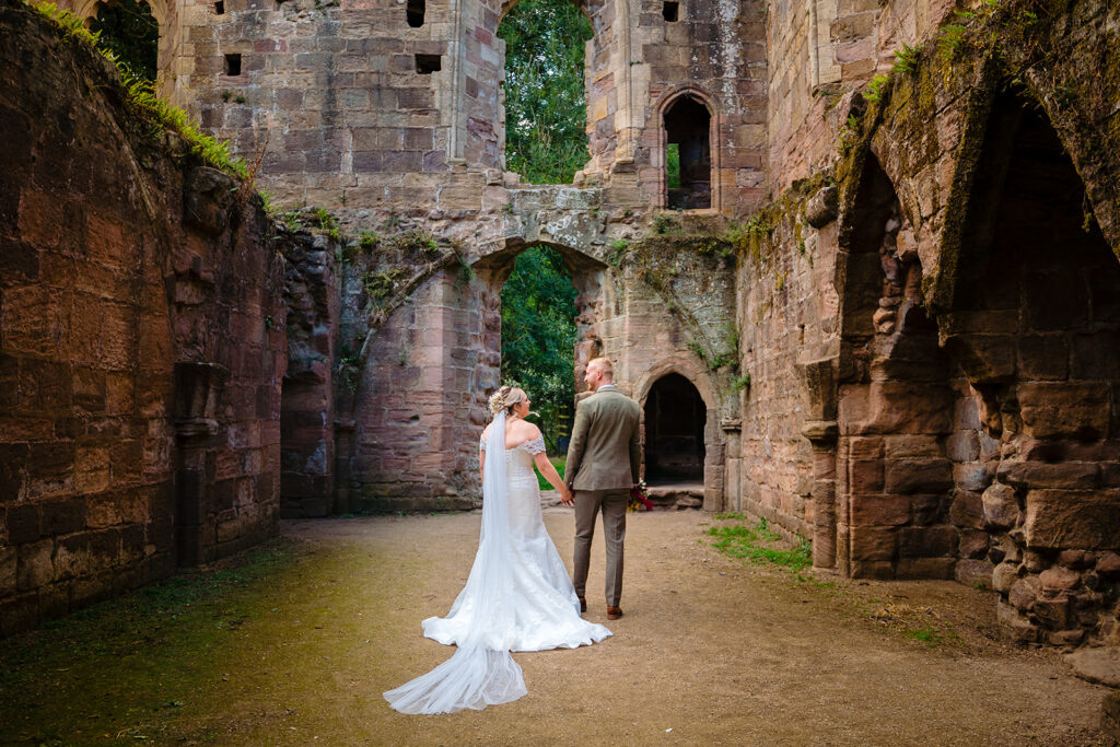 Bride and groom holding hands in historic stone castle ruins