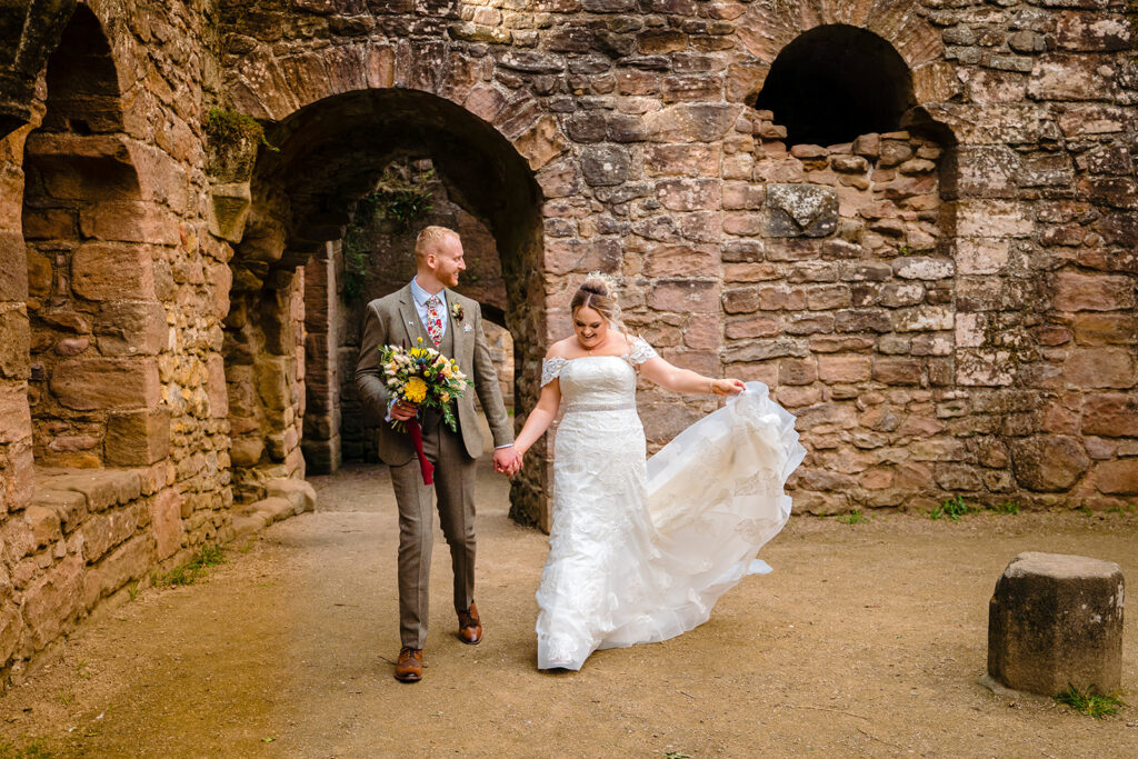 Bride and groom walking through historic stone archway ruins