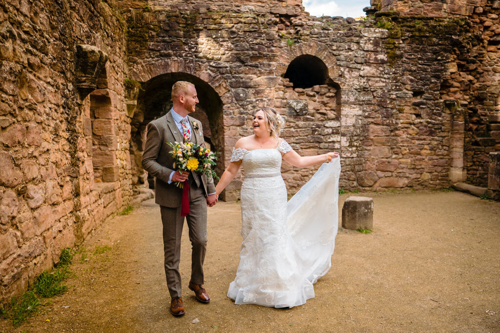 Bride and groom holding hands at historic stone ruins