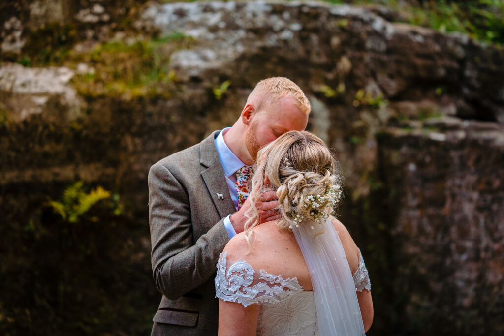 Groom kissing bride at rustic stone wall wedding venue