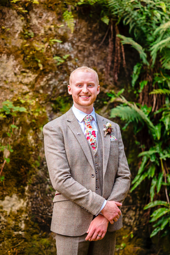 Groom in beige tweed suit against moss-covered stone wall