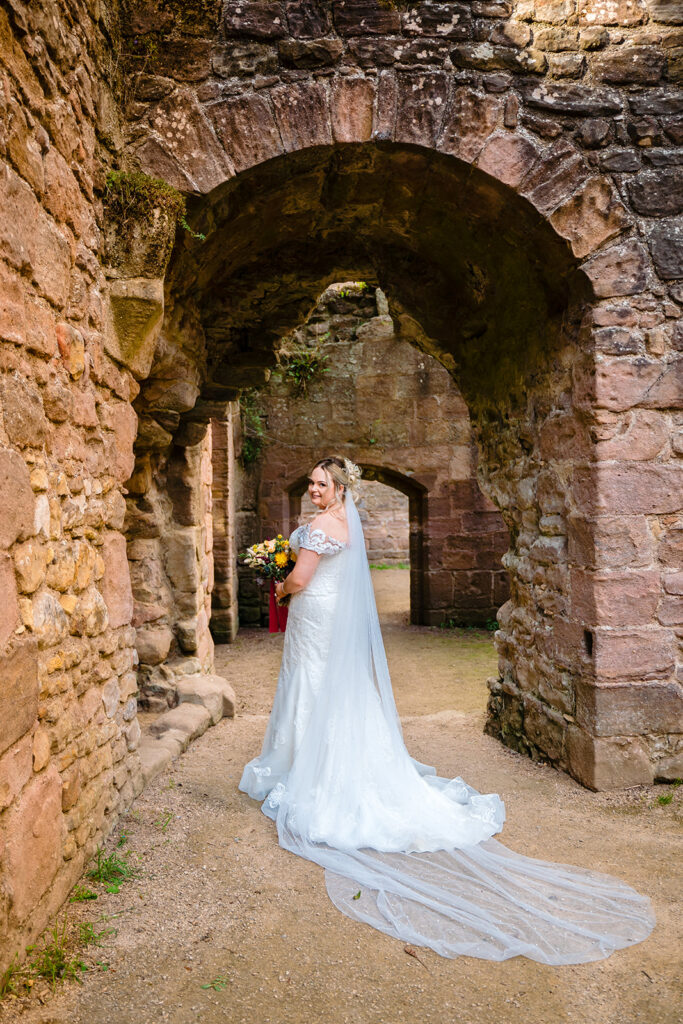 Bride in white dress posing in ancient stone archway