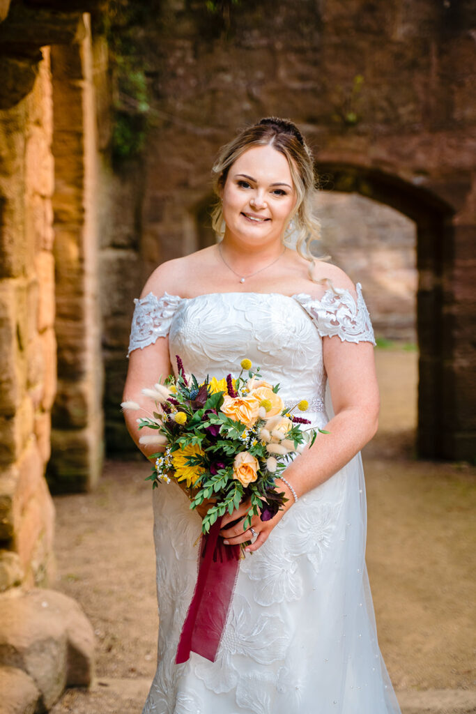Bride in white lace dress holding colourful bouquet outdoors