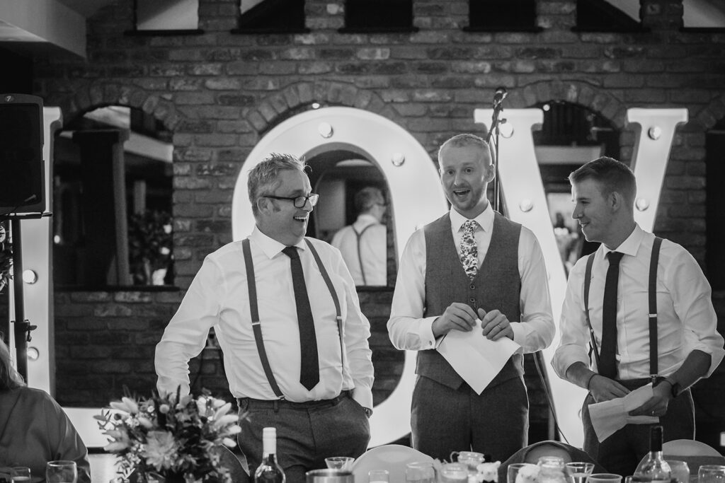Three men in formal attire laughing at wedding reception