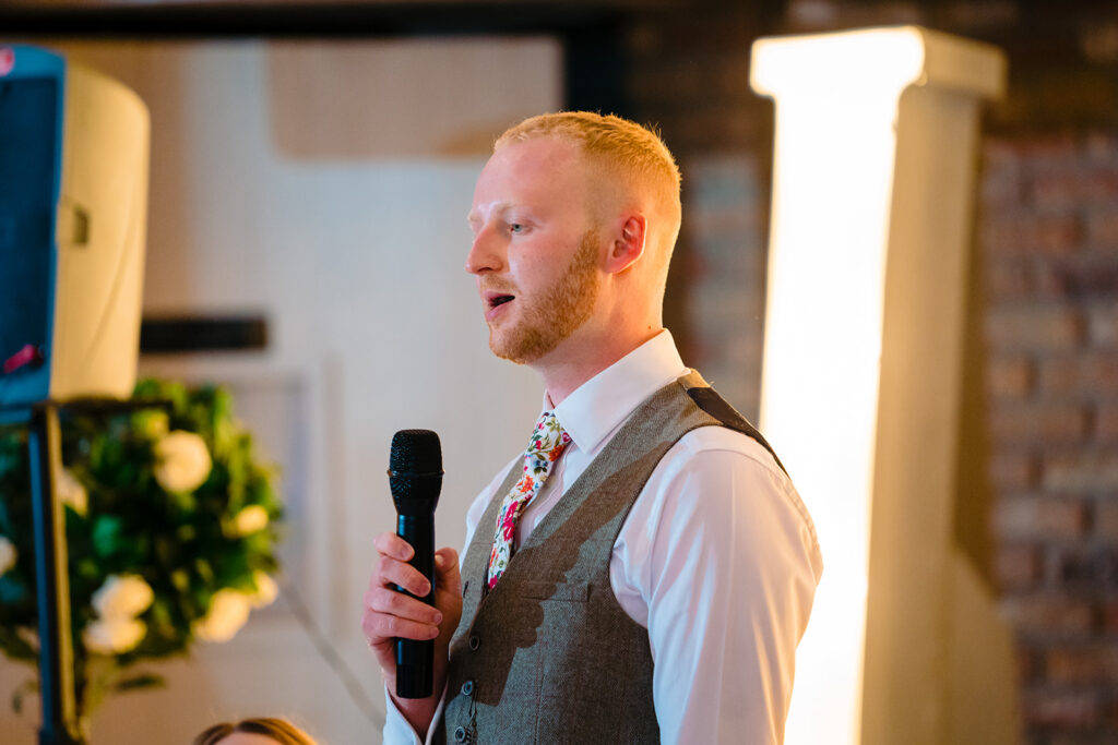 Man speaking at microphone wearing waistcoat and floral tie