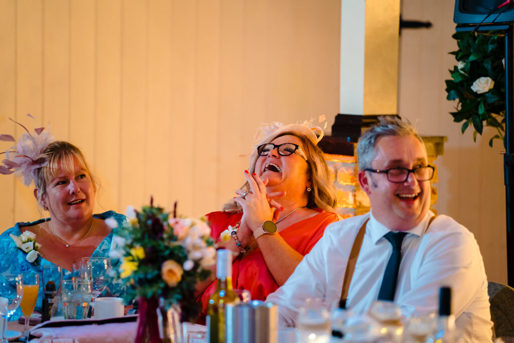 Three guests laughing at formal dinner table celebration