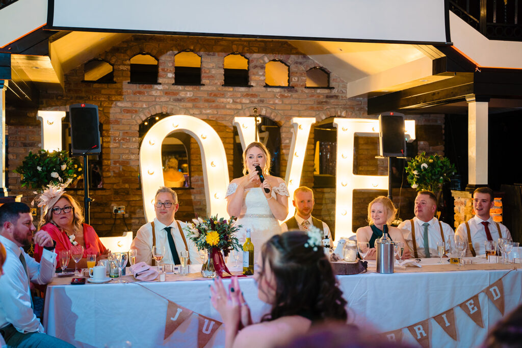 Bride speaking at wedding reception with illuminated LOVE sign backdrop