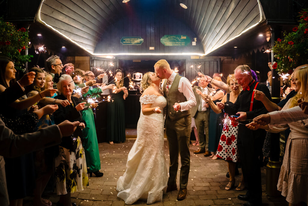 Bride and groom kiss surrounded by guests holding sparklers at night