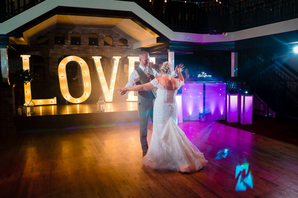 Bride and groom dancing at wedding reception with LOVE sign