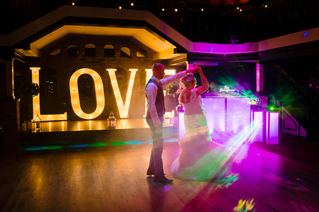 Bride and groom dancing beneath illuminated LOVE sign at night