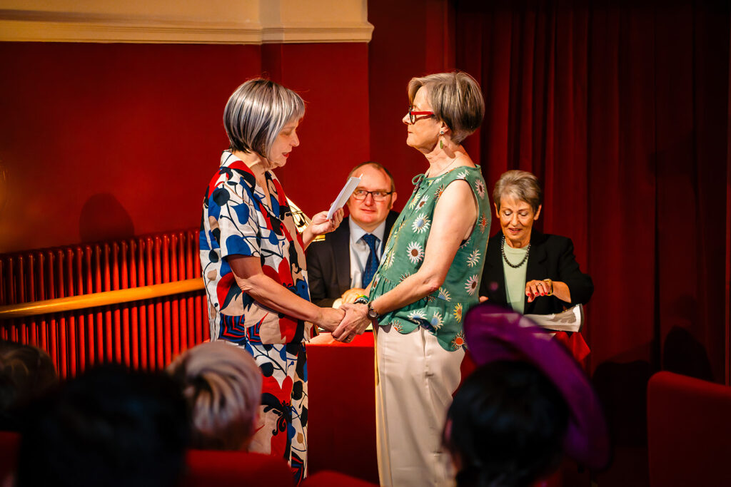 Beverly and Jane facing each other during their vows, with the registrars and a witness behind them