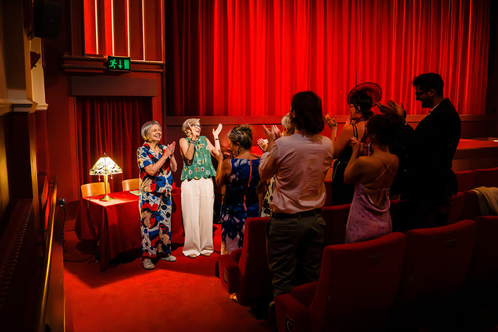 Guests standing and applauding Beverly and Jane in the red auditorium of the Hyde Park Picture House
