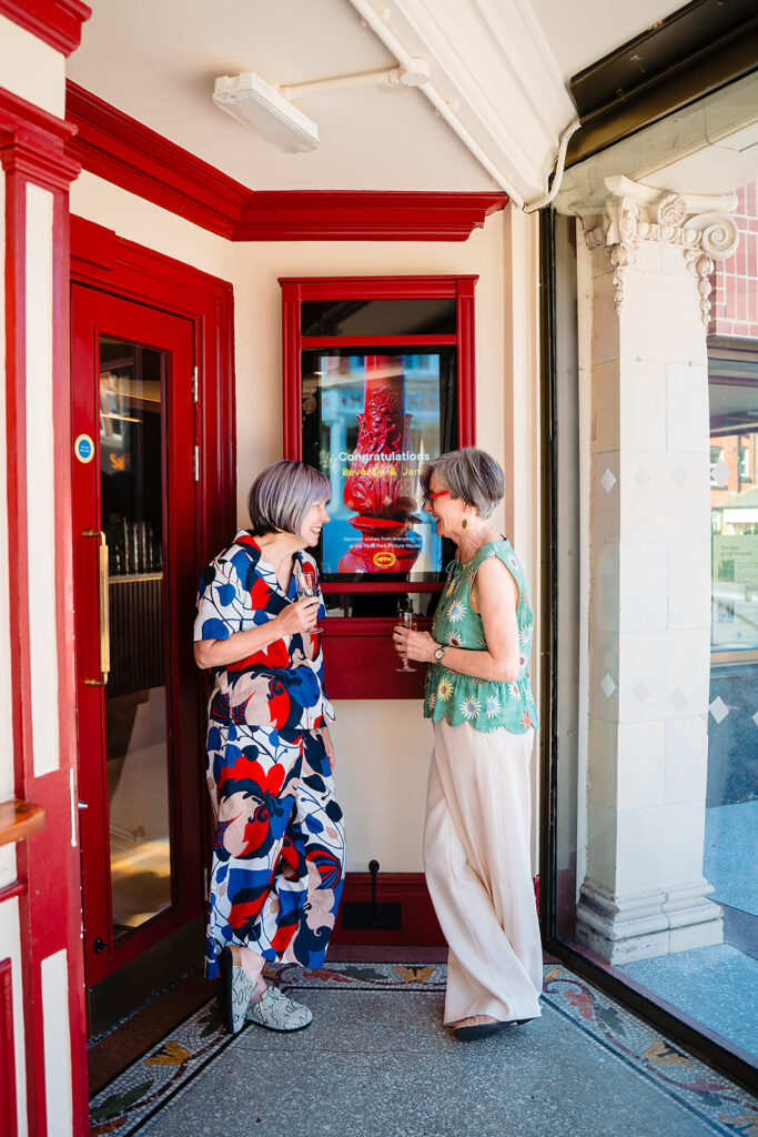 Beverly and Jane by the red ticket booth at the entrance of the Hyde Park Picture House