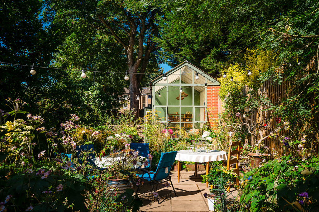 A garden party set up with tables, festoon lights and a glasshouse among summer flowers in Leeds
