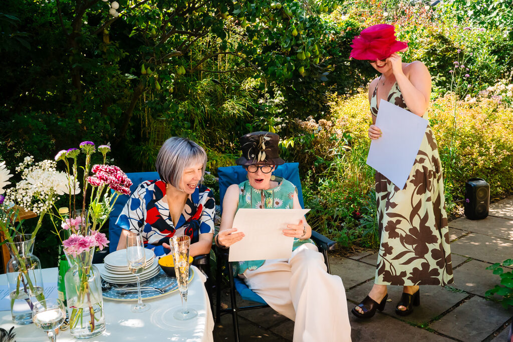 Beverly and Jane laughing as they open a present in the garden from a friend in a pink hat