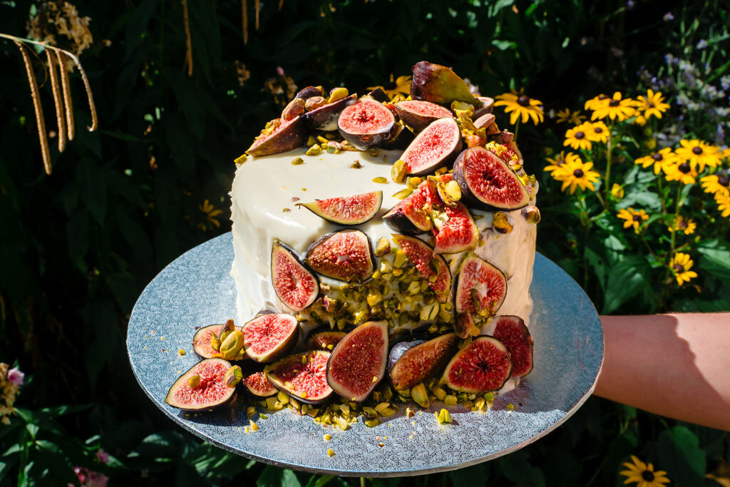 Wedding cake topped with fresh figs and pistachios, held up against garden flowers
