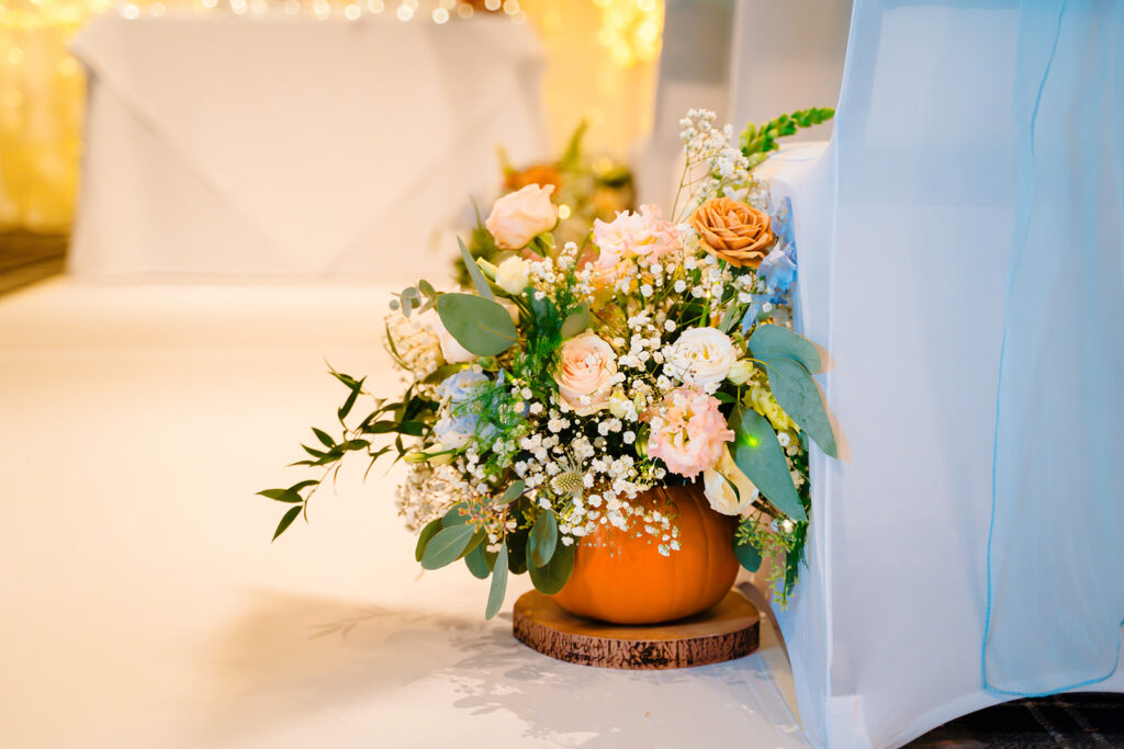 Peach, cream and blue wedding flowers arranged in a small pumpkin at the end of an aisle