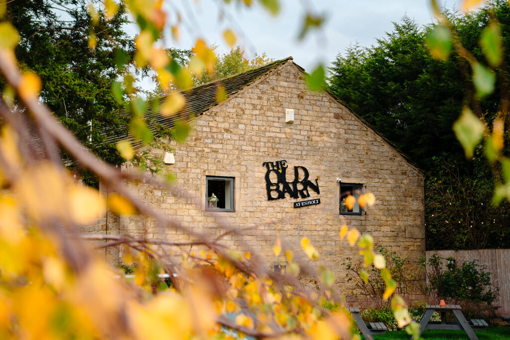The Old Barn at Esholt sign on the stone barn, framed by yellow autumn leaves