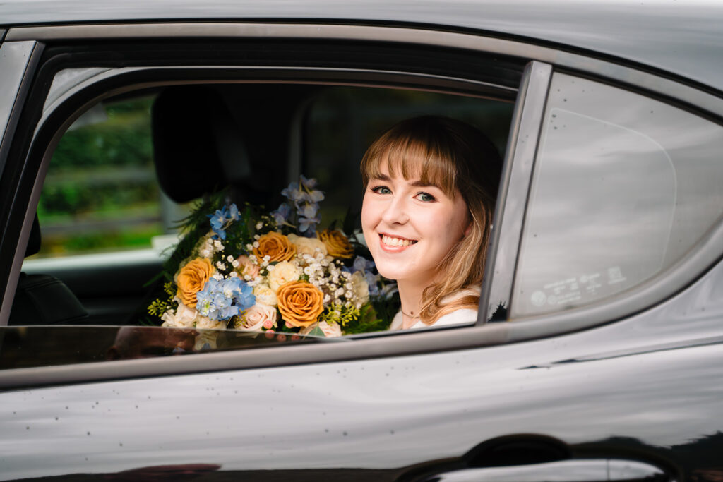 Cody smiling from the back window of the wedding car with her bouquet