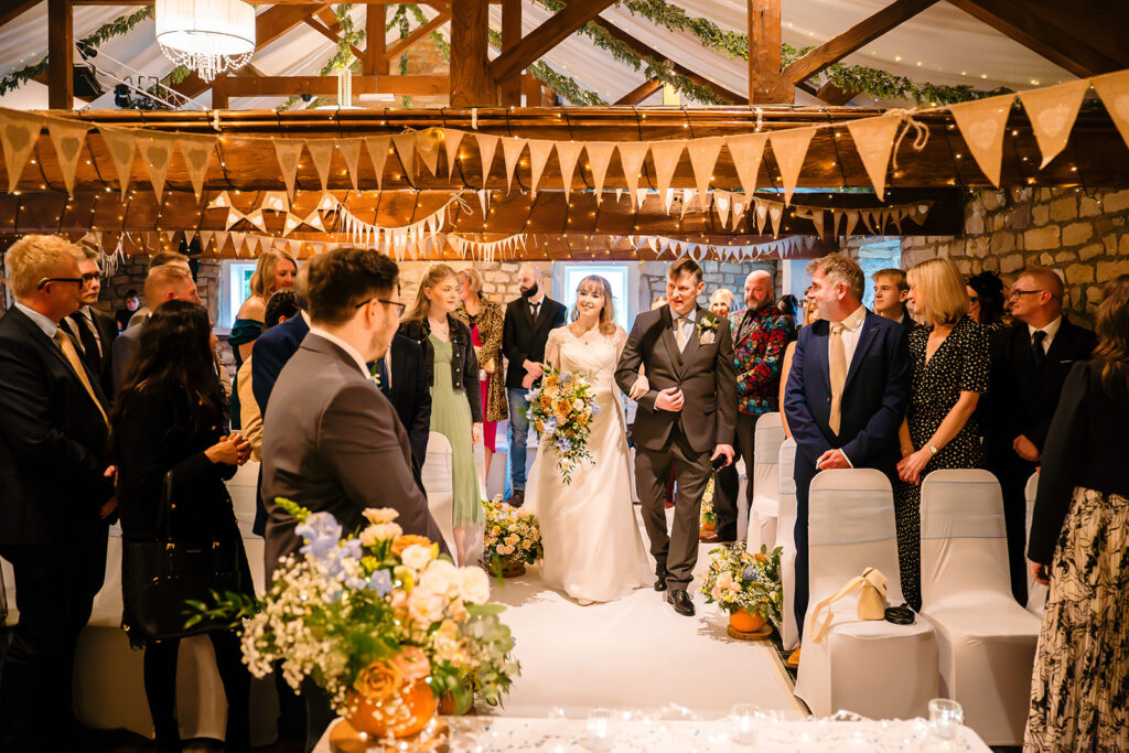 Cody walking down the aisle under bunting and fairy lights at The Old Barn at Esholt