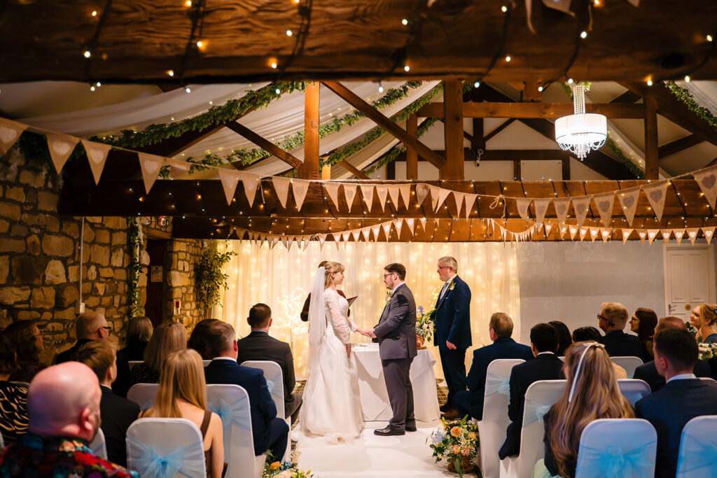 Cody and Dale holding hands during their vows in front of a wall of fairy lights