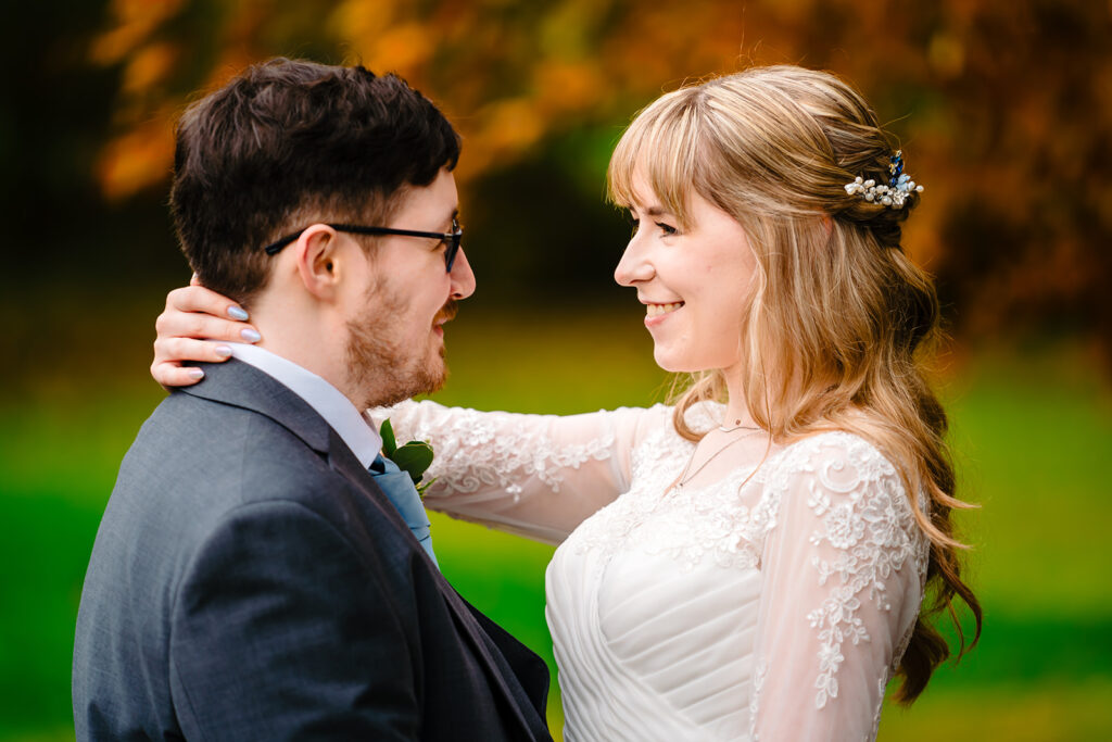 Cody and Dale embracing by a dry-stone wall under a bright orange autumn tree at The Old Barn at Esholt