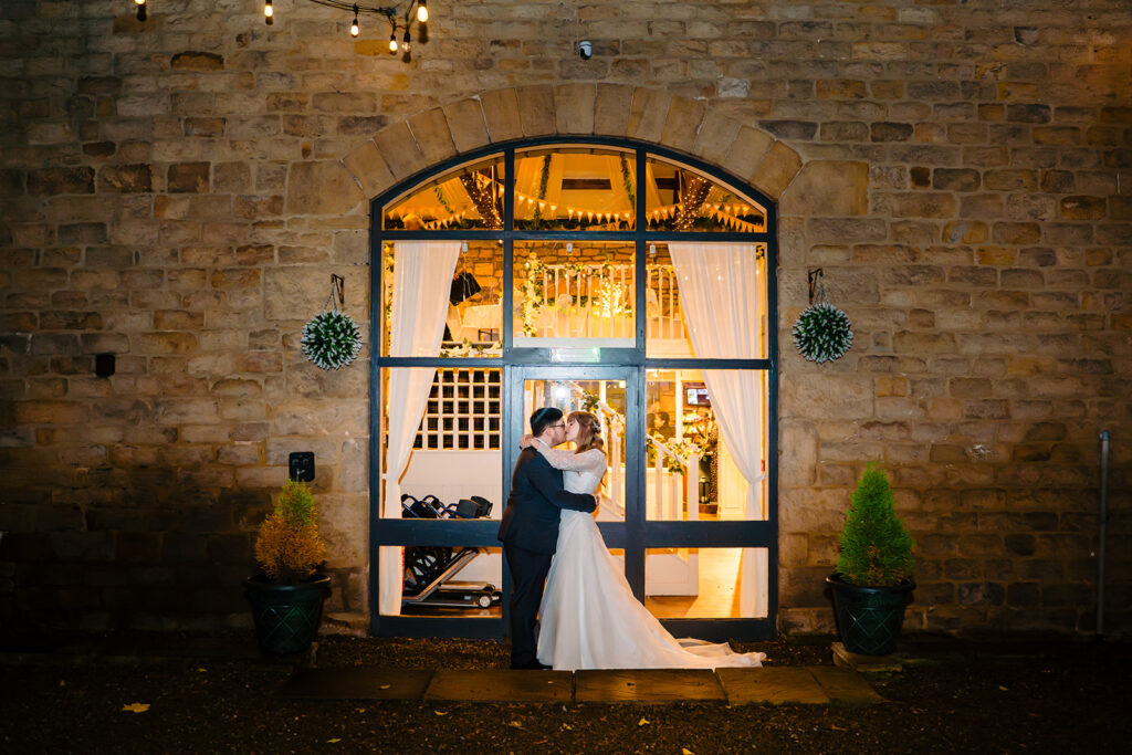 Cody and Dale kissing in the lit doorway of The Old Barn at Esholt at night