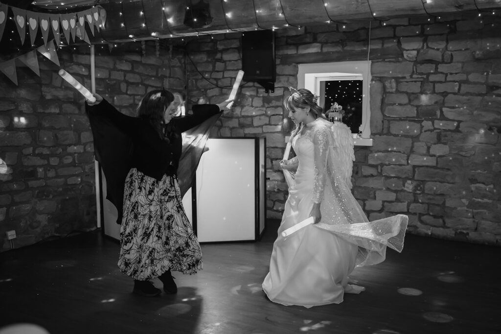 Black and white photo of Cody in angel wings dancing with a guest waving glow sticks
