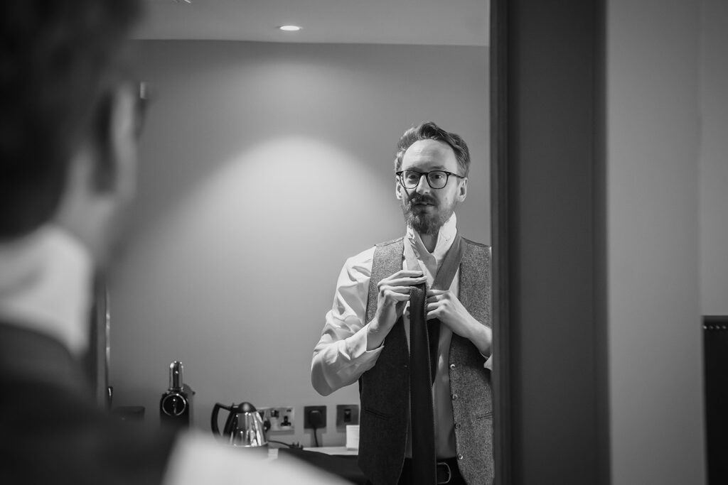 Black and white photo of Anthony fastening his tie in the mirror while getting ready at the Grand Hotel, York