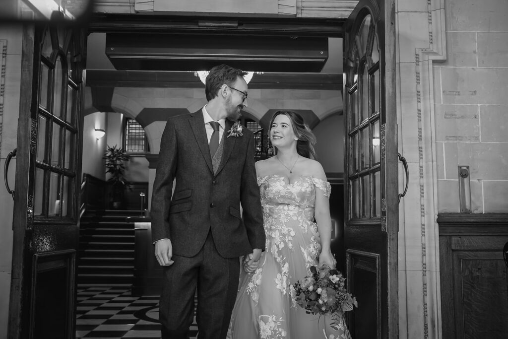 Black and white photo of Ellissa and Anthony walking out together through the doors of the Grand Hotel, York