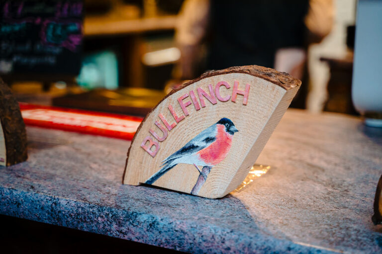 Hand-painted bullfinch table name on a wooden slice at Fran and Andy's goldfinch-themed wedding