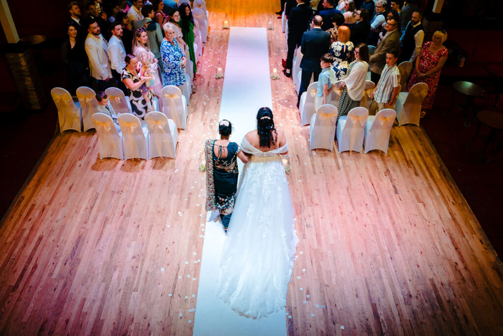Fran walking down the aisle with her mum, photographed from the mezzanine of the Engine Shed