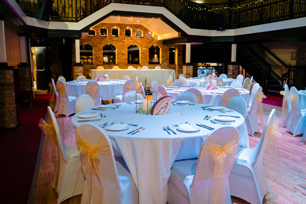 The Engine Shed's main room set with round tables for Fran and Andy's wedding breakfast, with the mezzanine above