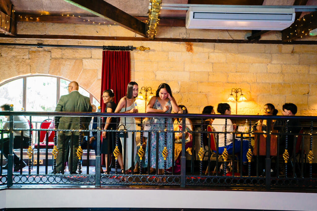 Wedding guests chatting at the railings of the Engine Shed mezzanine bar during the drinks reception