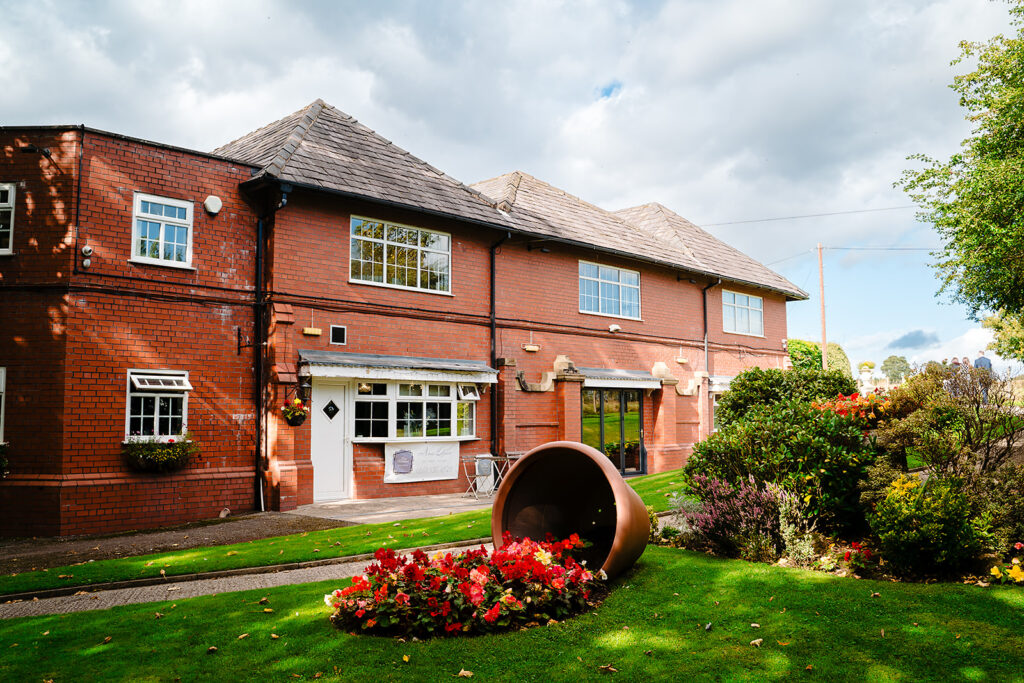 The red-brick front of the Stables Country Club in Bury, with flower beds on the lawn