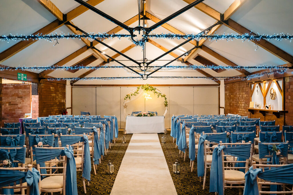 The Horseshoe Barn set for the ceremony, with dusty-blue chair sashes, fairy lights and a floral arch