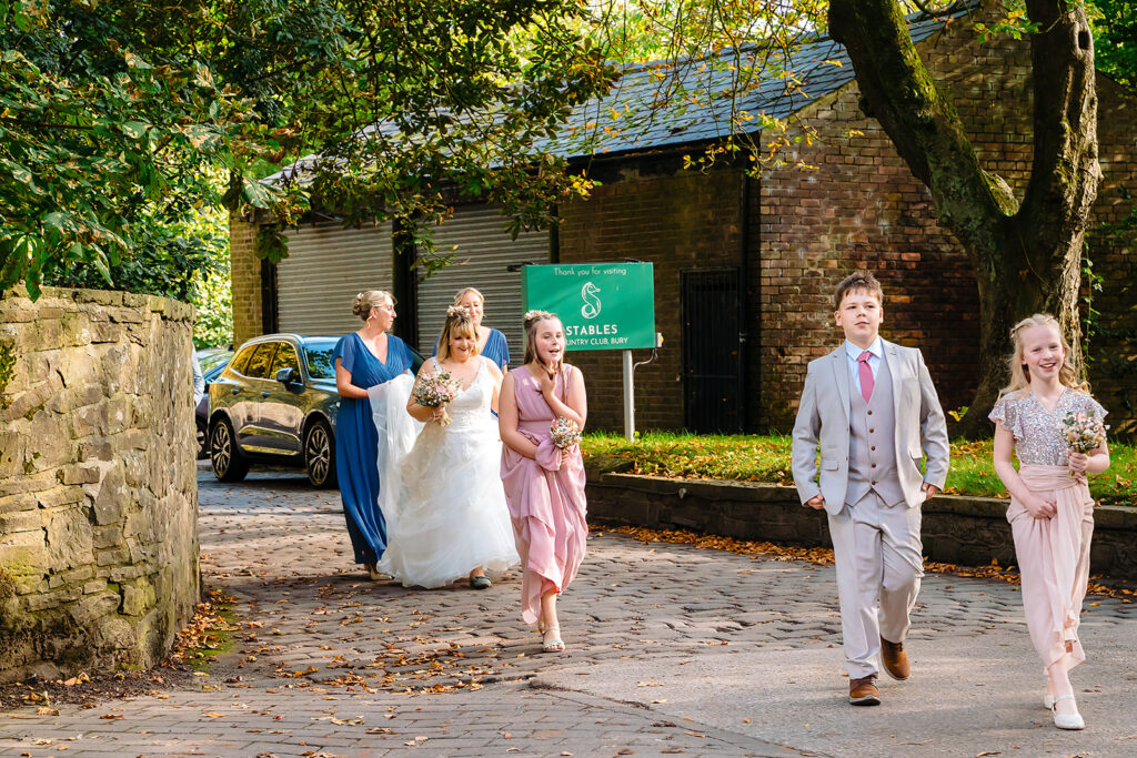 Kay arriving along a cobbled path with her bridesmaids, flower girls and son at the Stables Country Club